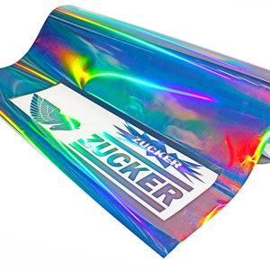 Può includere: Un rotolo di vinile blu iridescente con un effetto arcobaleno. Il vinile è arrotolato e ha un'etichetta con la parola "ZUCKER" stampata su di esso.