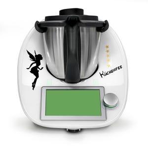 Op de afbeelding: Witte keukenapparaat met een zilveren kom, een zwarte handgreep en een digitaal display. Het apparaat heeft een zwarte fee-silhouet sticker aan de linkerkant en de tekst "Küchenfee" aan de rechterkant.