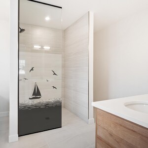 Peut inclure: Une cabine de douche moderne avec une porte vitrée ornée d'une scène nautique en noir et blanc. Le motif comprend un voilier sur l'eau avec des mouettes volant au-dessus. La zone de douche a des murs carrelés de couleur claire et un plafond blanc.