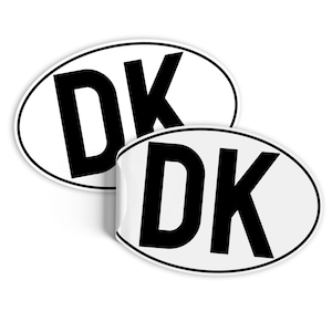 Może przedstawiać: Dwa białe owalne naklejki z czarnym napisem. Każda naklejka zawiera napis "DK" pogrubionymi, czarnymi literami.
