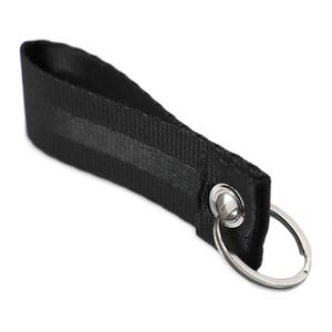 Könnte beinhalten: Schwarzer Schlüsselanhänger mit einem silbernen Ring und einem schwarzen Band mit einer silbernen Öse.