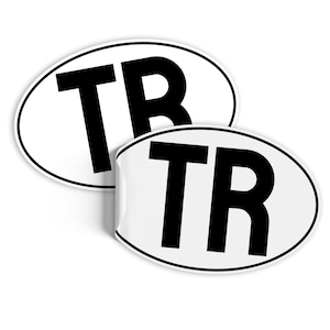 Może przedstawiać: Dwa białe owalne naklejki z czarnym napisem. Każda naklejka zawiera napis "TR" pogrubionymi, czarnymi literami.