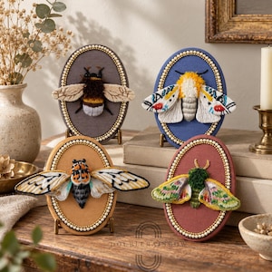 May include: Four oval embroidery hoops featuring insect designs. One shows a bumblebee on gray fabric, one a white moth with colorful patterns on blue, one a cicada on tan, and one a green and pink moth on maroon. Each hoop has a beaded border.