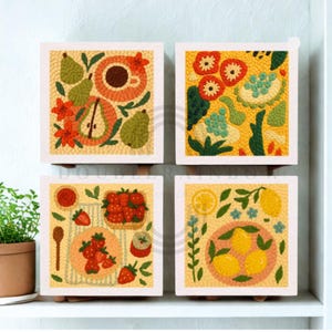 Op de afbeelding: Vier vierkante wandkunstwerken met geborduurde ontwerpen. De kunst toont afbeeldingen van fruit, waaronder peren, aardbeien en citroenen, samen met een kopje koffie. Het kunstwerk staat tegen een lichtgele achtergrond met een witte lijst.