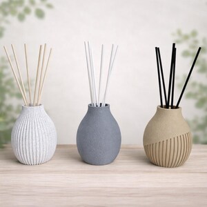 May include: Three decorative reed diffuser sets. Each set includes a ceramic vase and reed sticks. The vases are white, gray, and tan, with varying textures. The reed sticks are natural, white, and black.