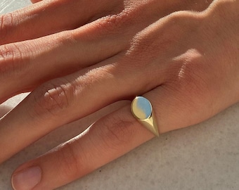 Könnte beinhalten: Ein goldener Siegelring mit einer glatten, ovalen Oberseite. Der Ring wird am Ringfinger einer Hand getragen.