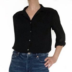 May include: A black long-sleeved button-down shirt with a collared neckline. The shirt is tucked into a pair of blue jeans.