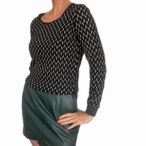 May include: A black and white patterned long-sleeved sweater with a round neckline. The sweater is paired with a dark green leather skirt.