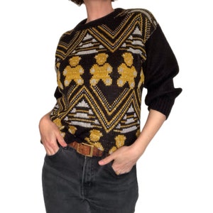 May include: A black and gold sweater with a geometric pattern and bear silhouettes. The sweater has long sleeves and a crew neck.