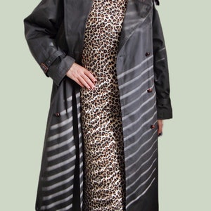 May include: A long, gray trench coat with white stripes. The coat has a double-breasted closure and a belt. The coat is worn over a leopard print dress.