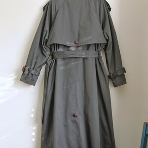 May include: A long, dark green trench coat with a belt and a button closure. The coat has a classic design and is made of a durable fabric.