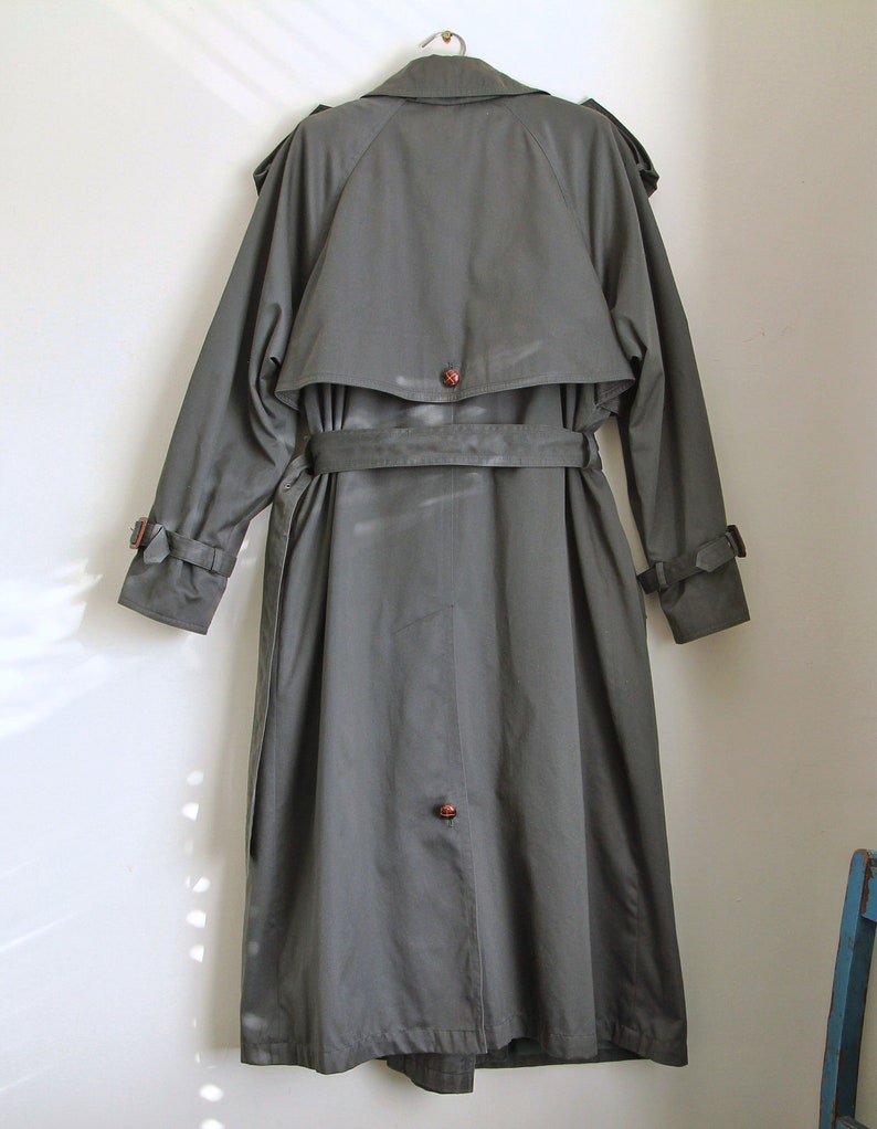 May include: A long, dark green trench coat with a belt and a button closure. The coat has a classic design and is made of a durable fabric.