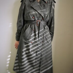 May include: A long, gray trench coat with a white striped pattern. The coat has a belt and a double-breasted closure.