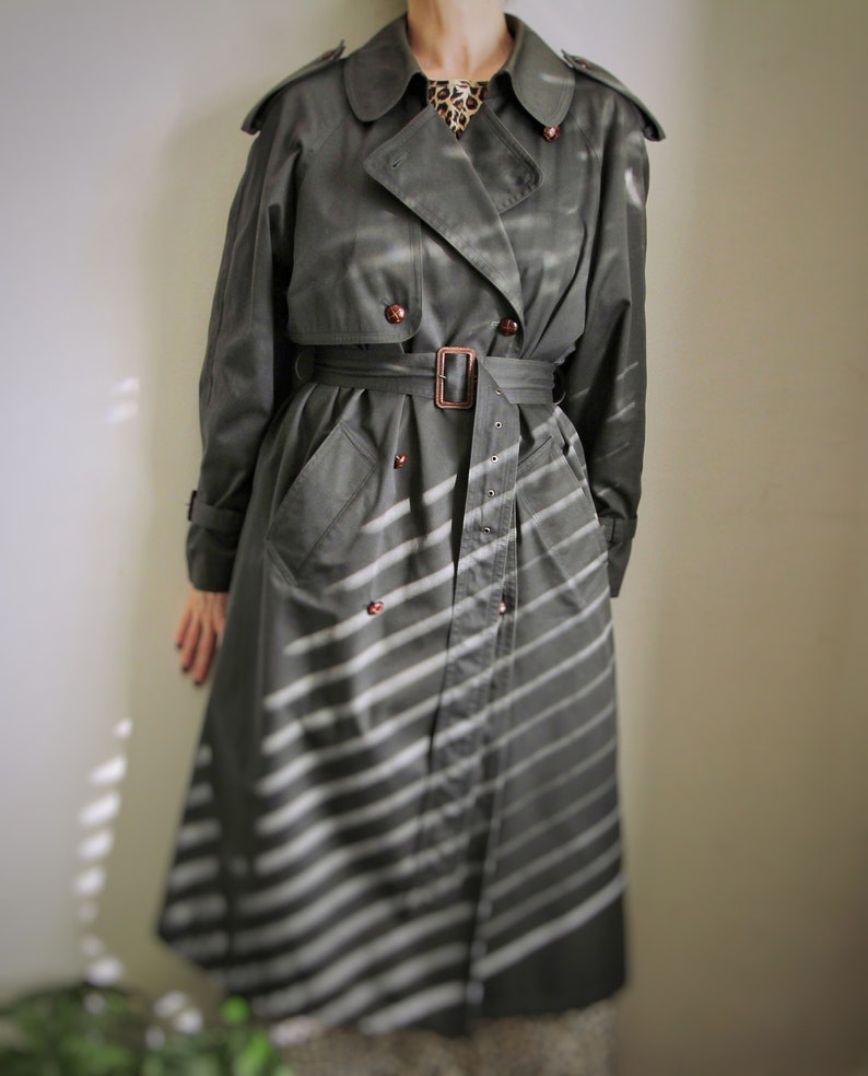 May include: A long, gray trench coat with a white striped pattern. The coat has a belt and a double-breasted closure.