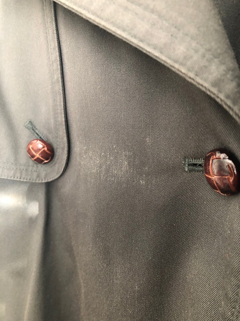 May include: Close-up of a dark gray fabric with two brown buttons. The buttons have a woven design and are sewn onto the fabric.
