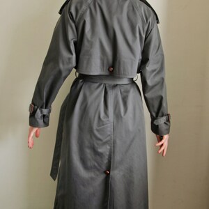 May include: A dark gray trench coat with a belt and a button closure. The coat has a classic design with a double-breasted front and a collar.