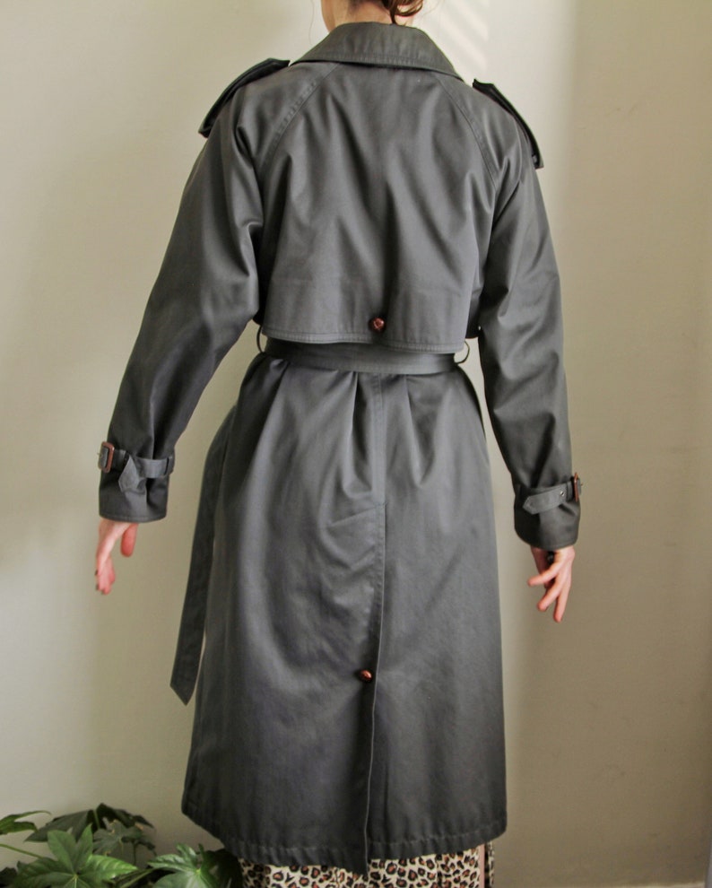 May include: A dark gray trench coat with a belt and a button closure. The coat has a classic design with a double-breasted front and a collar.
