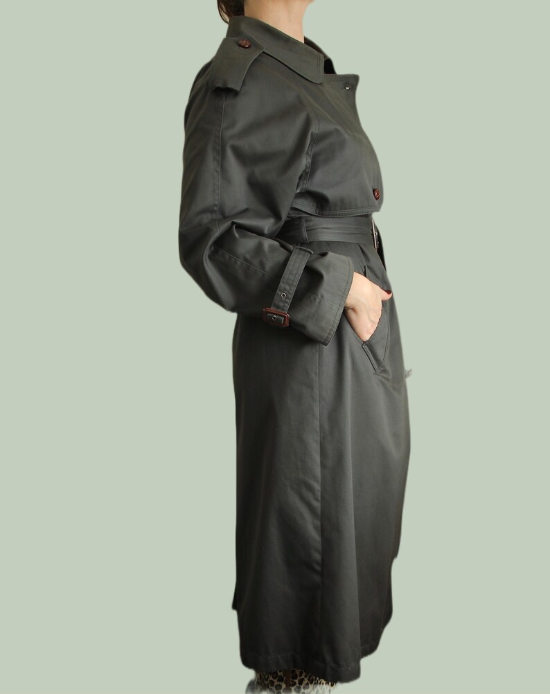 May include: A long, dark green trench coat with a belt and a button closure. The coat has a classic design with a collar and pockets.