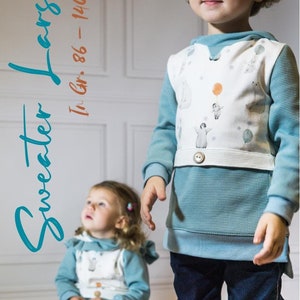 Op de afbeelding: Twee kinderen dragen blauwe en witte sweatshirts met een pinguïn- en ballonontwerp. De trui heeft een witte band met een knoop op de taille. De tekst "Sweater Lambs" staat in blauw en oranje aan de linkerkant van de afbeelding. De tekst "In Gr. 86 - 140" staat in oranje aan de rechterkant van de afbeelding.
