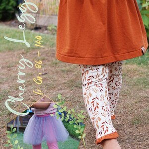 May include: A young girl wearing a brown skirt and white leggings with a brown leaf pattern. The leggings have a brown ruffle at the bottom. The text "Cherry Leggings" is written in a cursive font in the top left corner of the image. The text "11 Gr. 86 - 140" is written in a cursive font in the top left corner of the image. The text "auch ohne Rock" is written in the bottom left corner of the image.