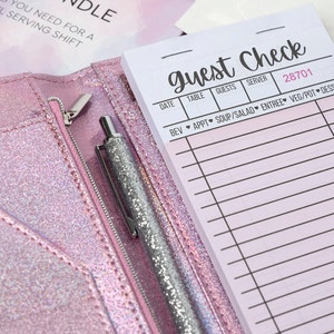 May include: A pink glittery server book with a notepad that says "Guest Check". A silver glitter pen is in the zippered pocket. The notepad has lines for taking orders. The server book is open.