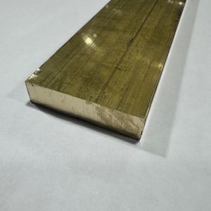 May include: A rectangular brass bar with a brushed finish. The metal bar is a golden color and has a flat, smooth surface. The edges are sharp and the bar is sitting on a white surface.