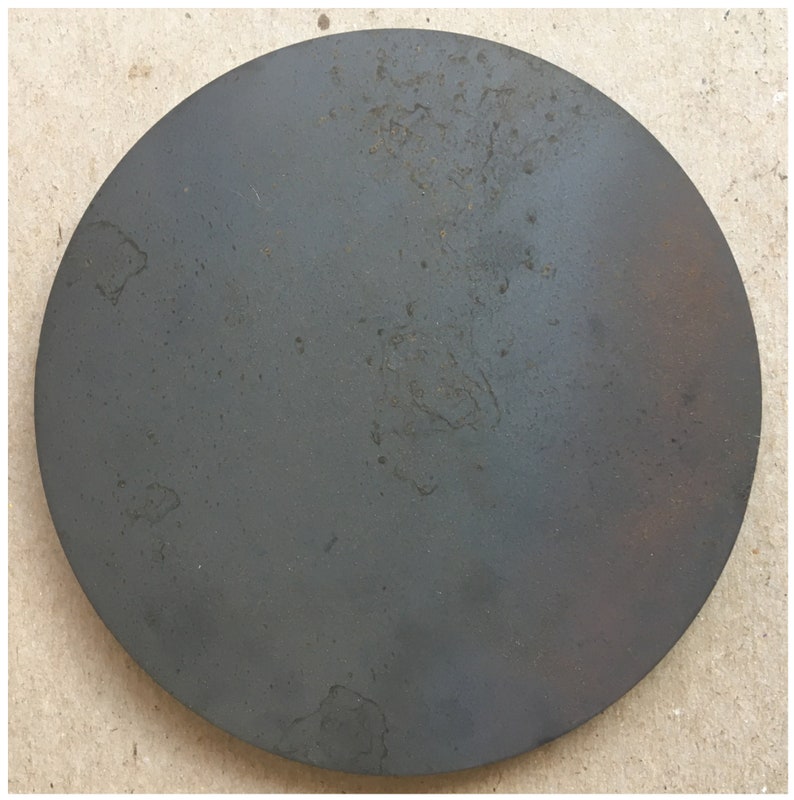 Puede incluir: Un disco redondo de metal gris oscuro con una superficie ligeramente texturizada. El disco tiene varias manchas peque&ntilde;as de color marr&oacute;n claro dispersas por su superficie.