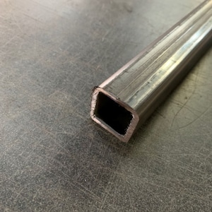 May include: Close-up of a silver metal square tube with a textured surface.