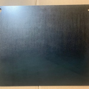 May include: A black metal plate with two holes in the top corners. The plate has a brushed finish.