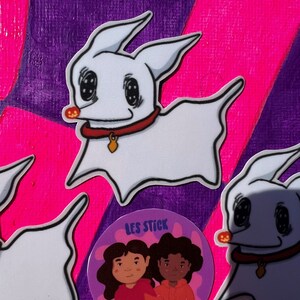 May include: Three stickers on a purple and pink background. Two stickers are white cartoon ghost dogs with black eyes and a red collar. The third sticker is a purple circle with two cartoon people with brown hair and brown skin. The text "LES STICK" and "2IT" are on the sticker.