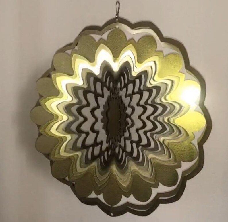 May include: A gold metal wind spinner with multiple layers of overlapping petals. The spinner is illuminated from within by a white light.