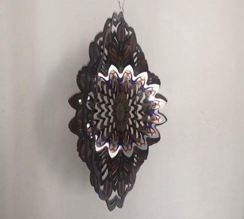 May include: A multi-layered metal wind spinner with a diamond shape. The spinner features a colorful, intricate design with shades of brown, white, blue, red, and gold.