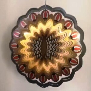 May include: A black metal wind spinner with a circular design. The center of the spinner features a swirling pattern of brown, gold, and black. The outer edge of the spinner is decorated with red and white striped circles.