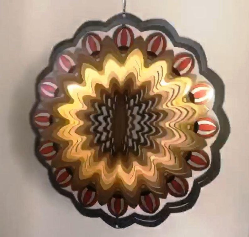 May include: A black metal wind spinner with a circular design. The center of the spinner features a swirling pattern of brown, gold, and black. The outer edge of the spinner is decorated with red and white striped circles.
