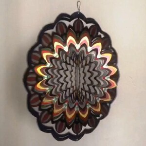 May include: A colorful metal wind spinner with a circular design. The spinner has multiple layers of overlapping metal pieces in shades of red, orange, yellow, green, and black. The center of the spinner is a black and white swirl pattern.