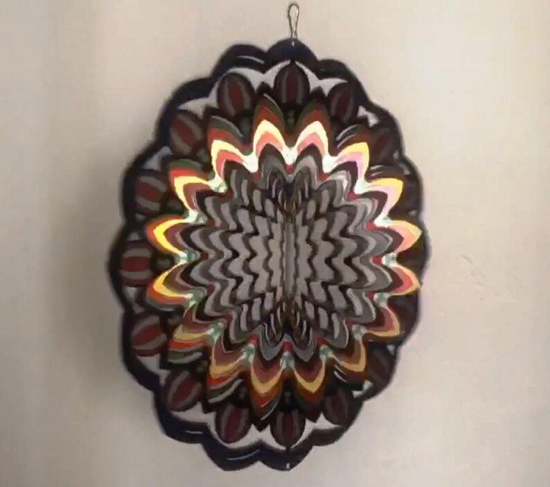 May include: A colorful metal wind spinner with a circular design. The spinner has multiple layers of overlapping metal pieces in shades of red, orange, yellow, green, and black. The center of the spinner is a black and white swirl pattern.