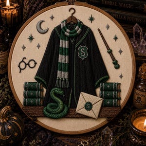 May include: A circular embroidery hoop featuring a black robe with a green and silver scarf, a green snake, a wand, round glasses, stacks of green books, and an envelope with a green wax seal, all stitched on a cream-colored fabric background.