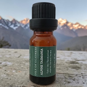 May include: A small amber glass bottle with a black ribbed cap and a green label. The label reads OILS OF GLADNESS, ALPINE TASMANIA, Take the Tasmanian alpine forest home, 1/3 oz | 10 ml, and Do not ingest. The bottle is cylindrical in shape.