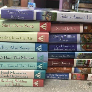 May include: A stack of paperback books with colorful spines. Titles include "Saints Among Us," "Sing a New Song," "Spring Is in the Air," and "They Also Serve." The books have various colors, including red, green, blue, and purple.