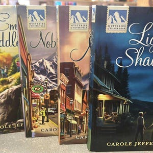 May include: A collection of four paperback books from the "Mysteries of Silver Peak" series. The book covers feature illustrations of landscapes and buildings. The book titled "Lights and Shadows" has a dark blue cover with the title in elegant script.