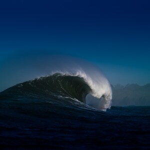 May include: A large wave curls over itself, creating a hollow tube against a dark blue sky. The wave is breaking in the ocean, with the water appearing dark and deep.