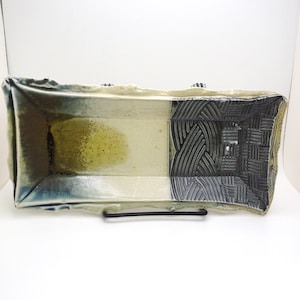 Op de afbeelding: Een rechthoekige keramische serveerschaal met een witte glazuur en een zwart-wit geometrisch patroon aan één kant. De schaal heeft een licht onregelmatige vorm en een getextureerd oppervlak.