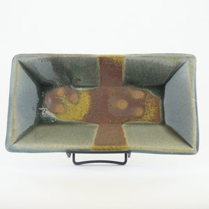 Op de afbeelding: Een rechthoekige keramische schaal met een groene glazuur en bruine en gele accenten. De schaal heeft een verhoogde rand en een licht getextureerd oppervlak.