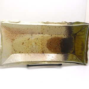 Op de afbeelding: Een rechthoekige keramische serveerschaal met een witte glazuur en bruine en groene accenten. De schaal heeft een licht onregelmatige vorm en een ruwe textuur.