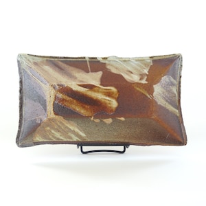 Op de afbeelding: Een rechthoekige keramische serveerschaal met een bruine glazuur en witte strepen. De schaal staat op een zwarte metalen standaard.