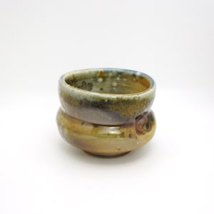 May include: A small, brown and green ceramic bowl with a unique, uneven shape. The bowl has a glazed finish and a speckled appearance.