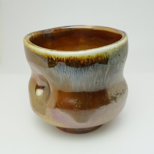 May include: A brown ceramic teacup with a white glaze and a textured surface. The cup has a rounded shape and a wide rim.