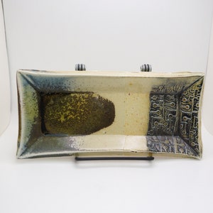 Op de afbeelding: Een rechthoekige keramische serveerschaal met een witte glazuur en bruine en zwarte accenten. De schaal heeft aan de ene kant een textuurontwerp en aan de andere kant een glad oppervlak.