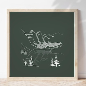 May include: A framed print with a white line drawing of a mountain scene on a dark green backdrop. The artwork depicts mountains, trees, and a lake. The frame is a light wood colour.