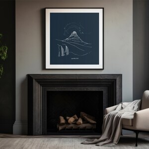 May include: A framed art print featuring a minimalist white line drawing of a mountain landscape on a dark blue background. The artwork is displayed above a black fireplace, with a beige armchair and a potted plant in the room.